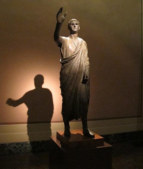 Image of the Arringatore statue, of an orator raising his right hand while giving a speech.