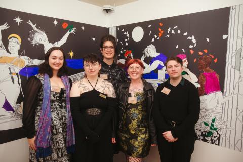 Five people stand smiling at the camera in front of a backdrop of illustrations of people in togas dancing