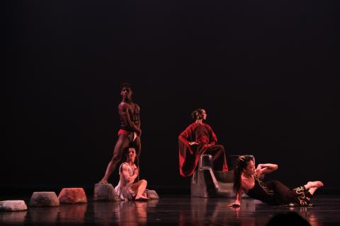 Four dancers pose on stage, one lying down, one sitting, one standing, and one kneeling. They look into the audience.