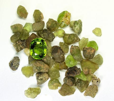 Small, dull lime green stones scattered in a pile. On top of them sits one shining, faceted gem stone in the same color green.
