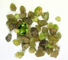 Small, dull lime green stones scattered in a pile. On top of them sits one shining, faceted gem stone in the same color green.