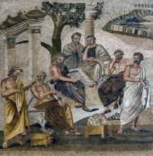 A group of men in togas sitting and standing outside near some columns and a tree