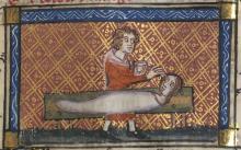 A medieval manuscript illustration with a red and gold patterned background. On it, a man holds a container in his left hand and with his right hand touches the face of a figure who is lying horizontally on a wooden table in front of him. The figure has a woman's head and face, but a formless body.