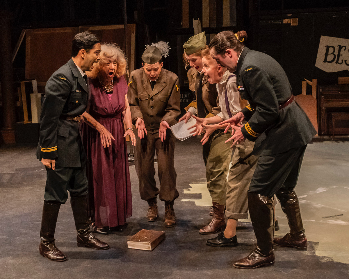 Six people stand in a semicircle around a book on the ground, their mouths open in a scream. From left: a man in military garb, and old woman in a mauve dress, two men in different military garb with hats, a person in pants with suspenders, and a man in military garb.