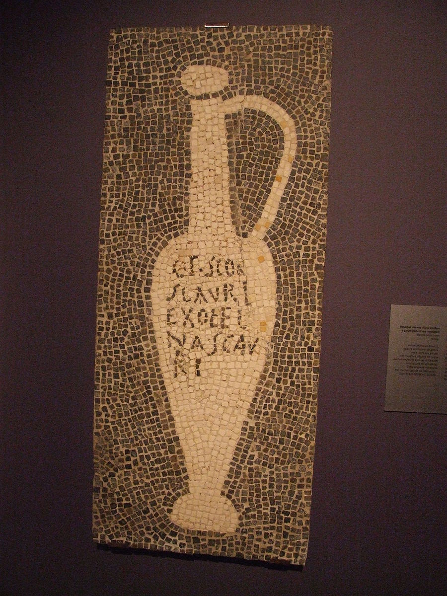A mosaic with a black background and a tall, narrow beige amphora with letters on it.