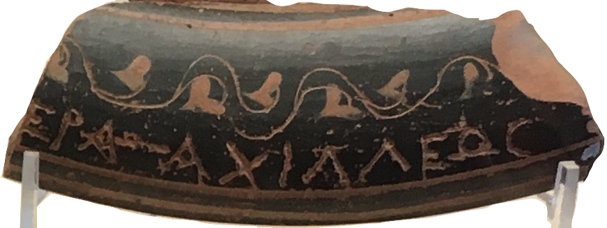 A black terracotta pottery sherd with a leaf motif and some Greek letters carved into it